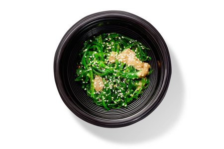 Photo for Traditional Japanese cuisine dish of spicy pickled hiyashi seaweeds served with peanut sauce and sesame seeds in black chawan, top view isolated on white background - Royalty Free Image