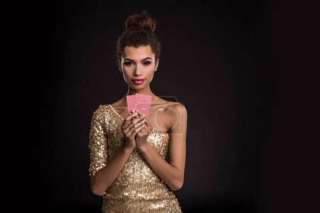 Foto de Mujer ganadora - Mujer joven con un elegante vestido de oro con dos cartas, una combinación de cartas de poker de ases. Estudio filmado sobre fondo negro. Emociones - Imagen libre de derechos