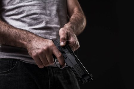 Photo for Killer with gun on black background at the studio. The man is holding a gun in his hand. Close-up. Bandit and thief - Royalty Free Image