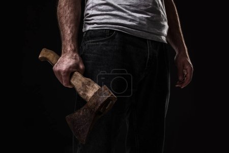 Foto de Un hombre sostiene un hacha en sus manos sobre un fondo negro. Criminal. - Imagen libre de derechos