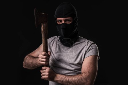 Foto de Bandido en máscara negra con hacha sobre fondo negro. Hombre enmascarado con un hacha - Imagen libre de derechos