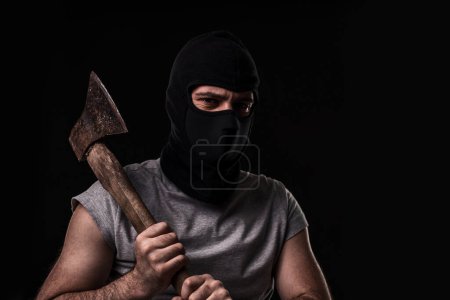 Foto de Bandido en máscara negra con hacha sobre fondo negro. Hombre enmascarado con un hacha - Imagen libre de derechos