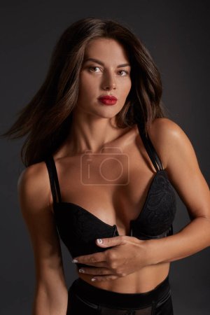 Téléchargez les photos : Stunning caucasian female model with dark hair and red lips in black underwear posing on dark grey background. Fashion portrait of young pretty beautiful brunette woman. - en image libre de droit