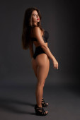 Young sexy slim tanned woman in black underwear posing against dark grey background. Fashion portrait of beautiful girl with long wavy brunette hair. Underwear or bikini model Sweatshirt #633367716