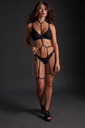 Beautiful woman in underwear and leather bandage. Sexy body girl weared swordbelt posing against dark grey background.