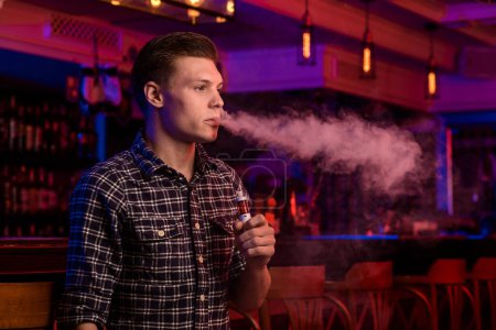 Photo for The man smoke an electronic cigarette at the vape shop. Vape bar. - Royalty Free Image