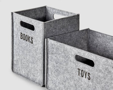 Two handcrafted bins in gray thick felt with handles for comfortable sorting and storage of things. Sides of boxes labeled Toys and Books in black letters. Artisanal interior accessories