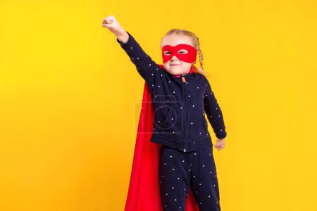 Foto de Niña superhéroe con un impermeable rojo y una máscara sobre un fondo amarillo. Estudio fotografía - Imagen libre de derechos