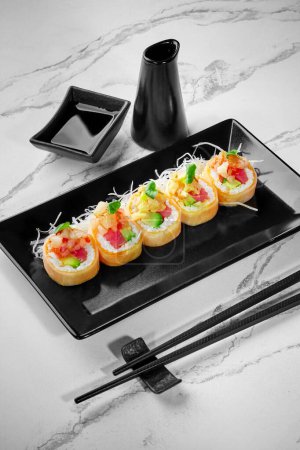Photo for Set of appetizing rolls in mamenori filled with salmon, tuna, avocado topped with sea scallop in sweet chili sauce served with shredded daikon and soy sauce on black plate. Popular Japanese style dish - Royalty Free Image