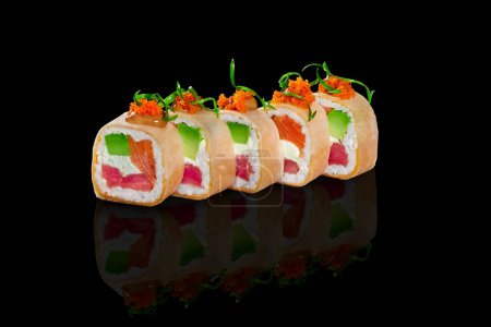Foto de Primer plano de rollos de sushi en mamenori rellenos de atún, salmón, aguacate y queso crema cubierto con salsa picante y tobiko en la superficie brillante negro con reflejo. concepto de comida japonesa - Imagen libre de derechos