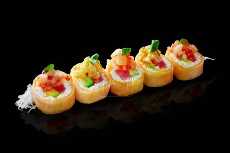 Foto de Exquisitos rollos de sushi envueltos en mamenori con relleno de salmón, atún y aguacate cubierto con vieira de mar en salsa de chile dulce servido con daikon rallado sobre fondo negro. Comida japonesa - Imagen libre de derechos
