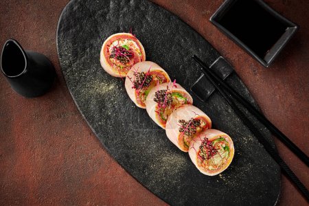 Foto de Rollos de sushi con carne de cangrejo, aguacate, lechuga y rodaja de naranja envueltos en atún, tortilla japonesa y papel de soja mamenori sin arroz adornado con tobiko negro espolvoreado con polvo dorado - Imagen libre de derechos