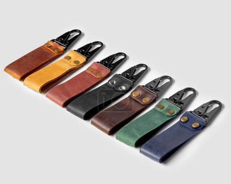 Collection of handcrafted embossed leather key holders in various colors with black durable metal carabiner clasps arranged in row against light background