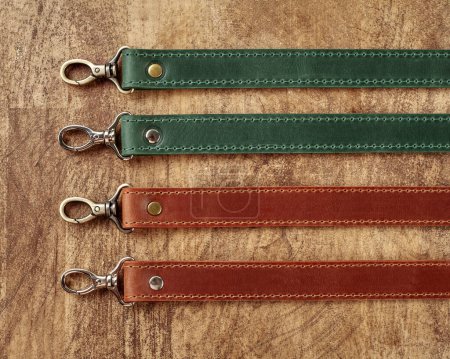 Collection of leather bag straps of different colors with metallic carabiners against wooden background, showcasing utility and craftsmanship