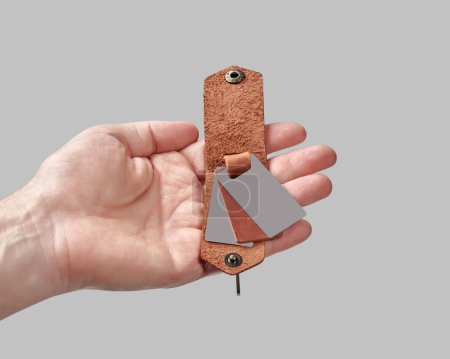 Close-up of male hand holding bespoke brown leather key holder adorned with printed family portrait against grey background, symbolizing personal and heartfelt gift