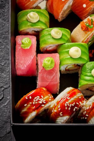 Buntes Set verschiedener japanischer Rollen mit Thunfisch, Lachs, Aal, Avocado und Masago-Rogen, garniert mit würzigem Mayo, Wasabi, verpackt in Karton, Draufsicht. Sushi-Lieferkonzept
