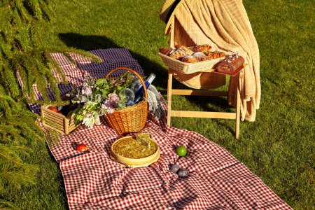 Gemütliche Sommer-Picknick-Szene auf grünem Gras mit hausgemachter Quiche, einer Flasche Wein im Weidenkorb und frischen Früchten verstreut auf karierter Decke, flauschigen Croissants und Schokoladenbrötchen auf Holzstuhl
