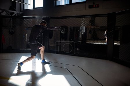 Photo for Dedicated male athlete engaging in shadowboxing session, simulating combat moves against imaginary opponent in boxing octagon cage in modern gym setting - Royalty Free Image