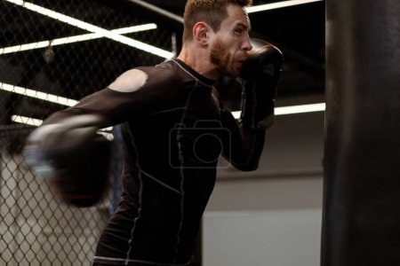 Photo for Determined young adult athlete throwing powerful right hook at heavy bag, showcasing power and form in dynamic workout at boxing gym - Royalty Free Image
