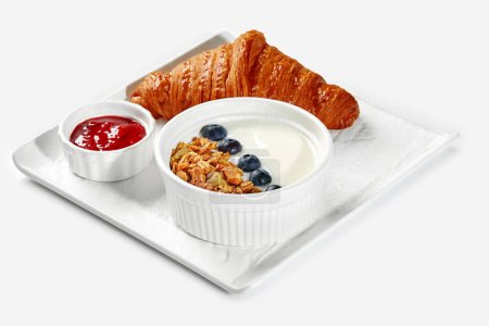 Téléchargez les photos : Croissant français floconneux classique, yaourt lisse au granola et aux bleuets frais, compote de baies maison servie comme petit déjeuner sur plateau blanc - en image libre de droit