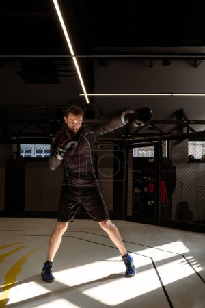 Photo for Concentrated boxer engaging in vigorous shadow boxing session in empty dimly gym, simulating fight to enhance strategic combat skills, improve punching technique and maneuvering - Royalty Free Image