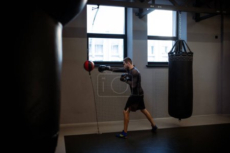 Photo for Focused athlete in boxing gym working on punching technique and speed with red and black double-end bag during training session - Royalty Free Image