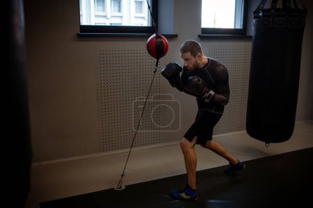 Photo for Determined concentrated boxer practicing coordination and punch control on red and black floor-to-ceiling bag during intense workout in modern gym - Royalty Free Image