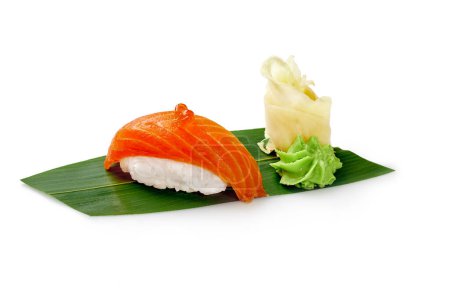 Delicious salmon nigiri sushi with roe, pickled ginger and wasabi served on green bamboo leaf isolated on white background. Traditional Japanese cuisine. Sushi bar menu concept