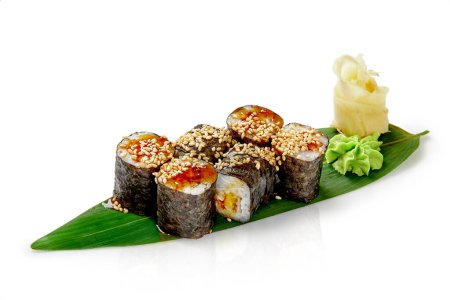 Rollos de sushi maki clásicos con anguila envuelta en arroz y nori rociados con salsa unagi y sésamo, servidos con jengibre en escabeche y wasabi sobre hoja de bambú, aislados en blanco. Auténtica cocina japonesa