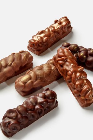 Variedad de barras de leche y chocolate negro con almendras, cacahuetes y avellanas, exhibidas sobre fondo blanco. Concepto de snack dulce popular
