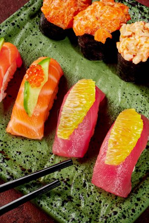 Photo for Delectable nigiri sushi with slices of fresh tuna and salmon, adorned with orange, cucumber, and caviar, served on speckled green plate with gunkan maki and chopsticks ready for Japanese style lunch - Royalty Free Image
