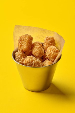 Mit Pergamentpapier ausgekleidete Metalleimer, gefüllt mit knusprigen Chicken Nuggets, präsentiert auf leuchtend gelbem Hintergrund. Konzept des beliebten Fast-Food-Snacks