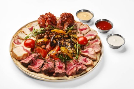 Delicious meat platter with roast beef slices, baked pork loin, grilled chicken breast and buffalo wings garnished with aromatic herbs, served with mix of grilled vegetables and variety of sauces