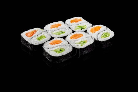 Conjunto de rollos futomaki en forma de yin y yang rellenos de salmón y pepino crujiente presentados sobre fondo negro. Cocina de estilo japonés