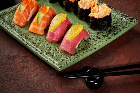 Photo for Vibrant sushi set of hand-tossed nigiri with tuna and salmon garnished with orange, cucumber and caviar, and gunkan maki with creamy fish and roe filling on mottled green ceramic plate with chopsticks - Royalty Free Image
