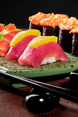 Appetitliches handgemachtes Nigiri-Sushi mit frischem Thunfisch und Zitrusfrüchten, serviert auf gesprenkelten grünen Keramiktellern mit Gunkan Maki mit Lachs und Tobiko-Füllungen. Japanische Küche