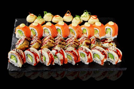 Lujoso juego de sushi crujiente tempura roll, norimaki al horno con tapas de queso y Filadelfia clásica con salmón y anguila rociada con salsa unagi y mayonesa servida en pizarra sobre fondo negro