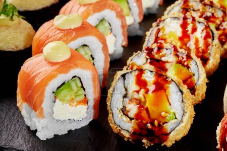 Großaufnahme von köstlichen, knusprigen Tempura-Rollen gefüllt mit Aal mit würziger Unagi-Sauce und Uramaki mit frischem Lachs und Tobiko gewürzt mit würzigem Mayo, serviert auf Schiefertafel. Japanische Küche