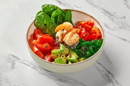 Delicious salad of plump fried shrimps resting on bed of sprouted seeds with avocado, tomatoes, bell peppers, spinach and hiyashi wakame, served in bowl on marble surface. Asian style cuisine