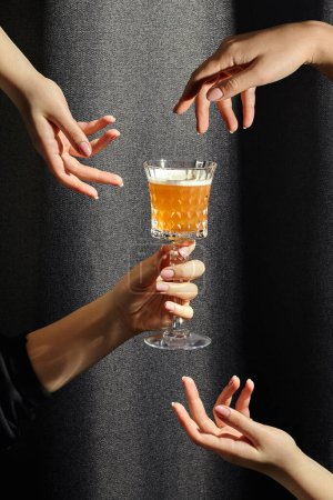 Las manos femeninas revoloteando elegantemente alrededor de un vaso de cristal de whisky agrio contra un fondo de tela de textura oscura con sombra. Concepto de espíritu de convivencia de compartir cóctel amado
