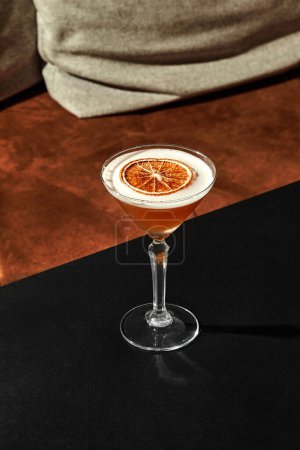 Elegant glass of almond sour cocktail with refreshing slightly sweet and tart flavor and frothy top decorated with dried grapefruit slice, presented on black surface