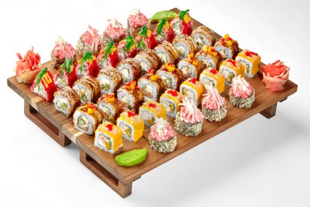 Buntes Set für große Unternehmen mit japanischen Sushi-Rollen mit Aal, Garnelen und Tobiko garniert mit verschiedenen Belägen, traditionell begleitet von eingelegtem Ingwer und würzigem Wasabi auf hölzernem Serviertablett