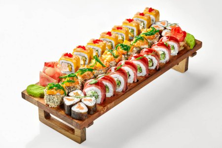 Colorido juego de sushi de deliciosos rollos tempura, uramaki y norimaki con salmón, atún y queso, cubierto con tobiko, wakame y verduras, servido con wasabi y jengibre en bandeja de madera sobre fondo blanco