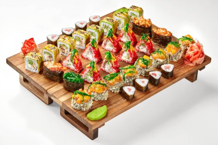 Colorful Japanese style party set with crispy tempura rolls, salmon norimaki, uramaki with eel, tobiko, avocado and gunkan maki with various toppings served with wasabi and ginger on wooden tray