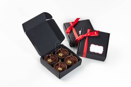 Exquisite Pralinen in Kaffeebecherform mit cremiger Füllung, verziert mit goldenen Kaffeebohnen, verpackt in schwarzen Geschenkboxen mit roten Bändern, ideal für besondere Anlässe