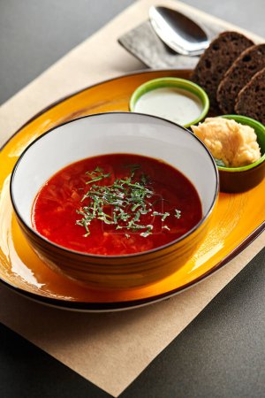 Hearty red borscht, traditional Ukrainian beet soup with cabbage and meat served in bowl with greens, sour cream, black bread and lard with garlic spread, served for lunch. National cuisine