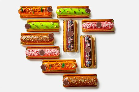 Variety of colorful eclairs with exquisite toppings of chocolate, nuts and fresh berries on golden cardboards arranged on white background, top view. Popular baked sweets concept