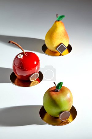 Various colorful sweet fruit shaped pastries with chocolate details served on golden cardboards against light background. Collection of signature desserts