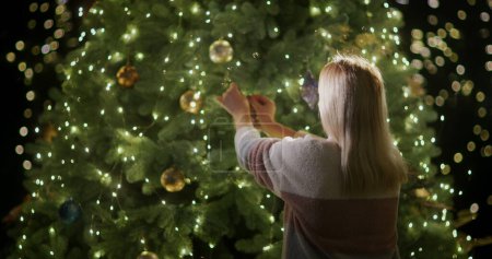 Foto de Una mujer decora un árbol de Navidad. Árbol de Navidad brilla con luces de guirnaldas. - Imagen libre de derechos