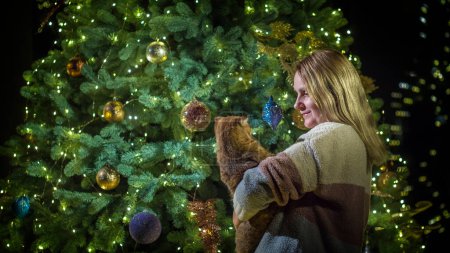 Téléchargez les photos : Une femme avec un chat dans les bras se tient sur le fond d'un magnifique sapin de Noël. Célébration de l'année du chat. - en image libre de droit